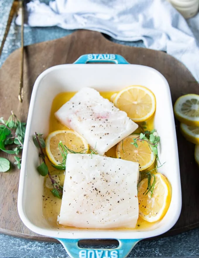 The seasoned halibut fish fillets are placed on top of the lemon garlic herb and butter layer on the baking dish