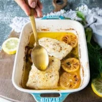 A hand scooping some of the butter from the bottom of the dish over the halibut to add even more butter flavor.