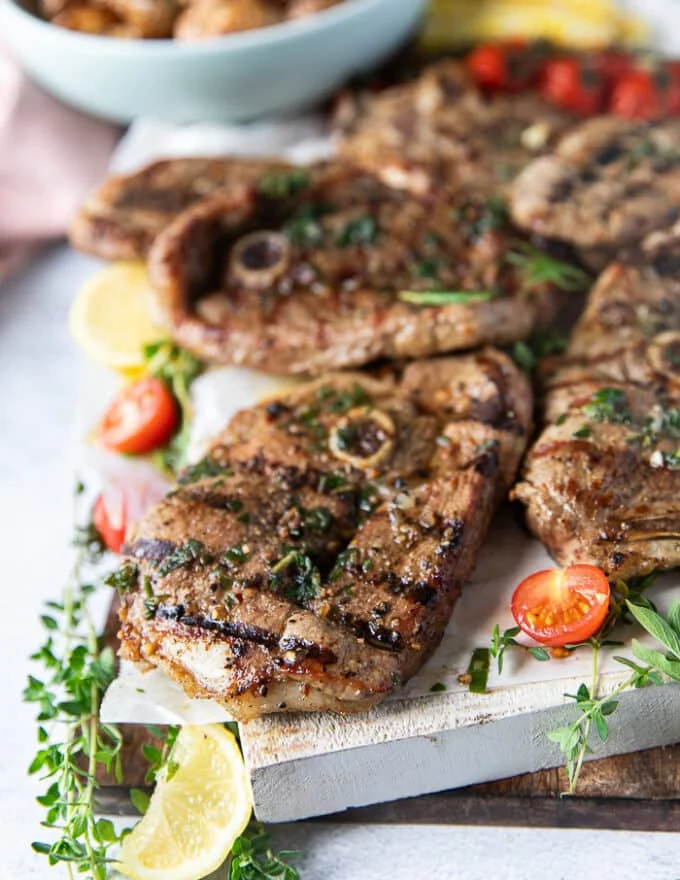 close up of one grilled lamb steak with herb butter and a lemon slice next to it along with fresh thyme