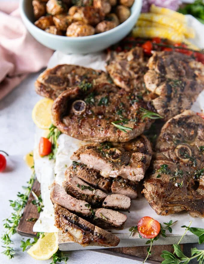 grilled lamb steaks on a platter with on steak sliced into strips to show the inside of the steak