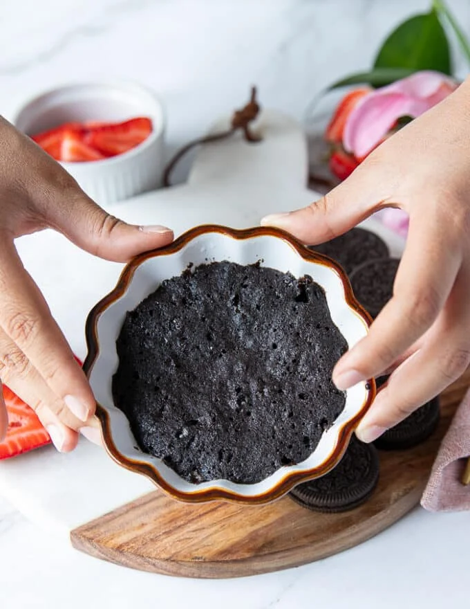 A hand holding the oreo mug cake right our of the microwave