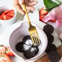 A hand holding a fork to start mashing the oreos with the ingredients to make oreo cake