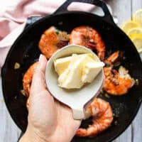 A hand holding chunks of room temperature butter in a small bowl ready to add them one at a time to make the sauce