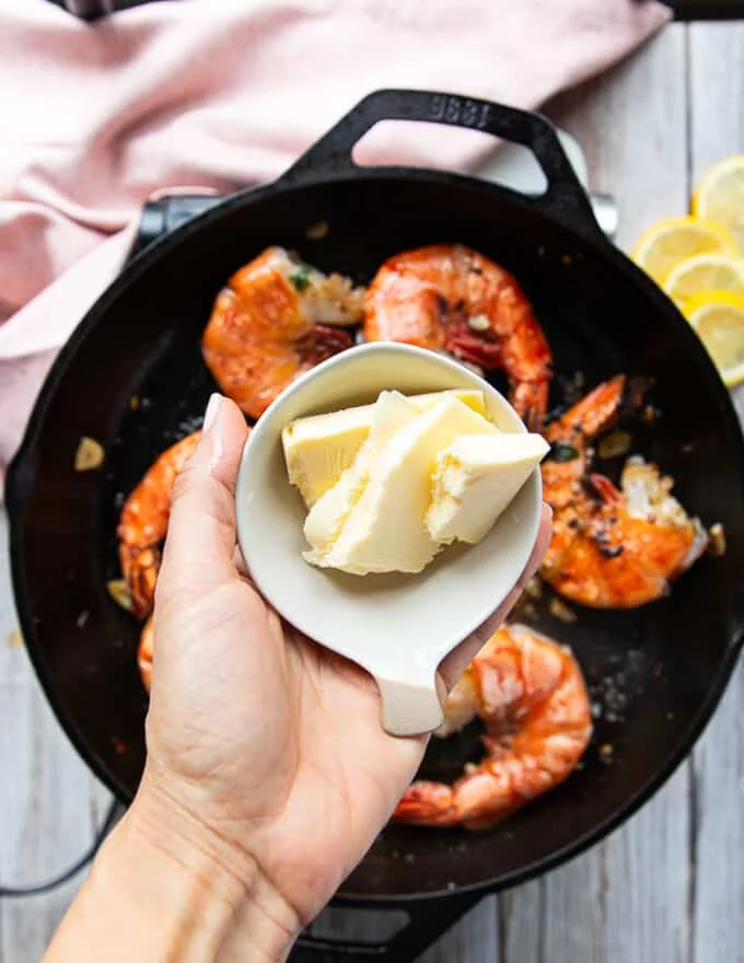 A hand holding chunks of room temperature butter in a small bowl ready to add them one at a time to make the sauce