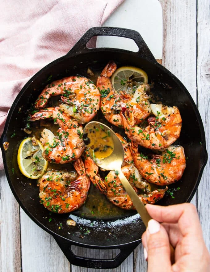 A hand holding a spoon showing the scampi sauce spooning it over the shrimp