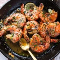 Shrimp scampi in a pan bathing in lemon garlic butter sauce and a spoon showing the scampi sauce