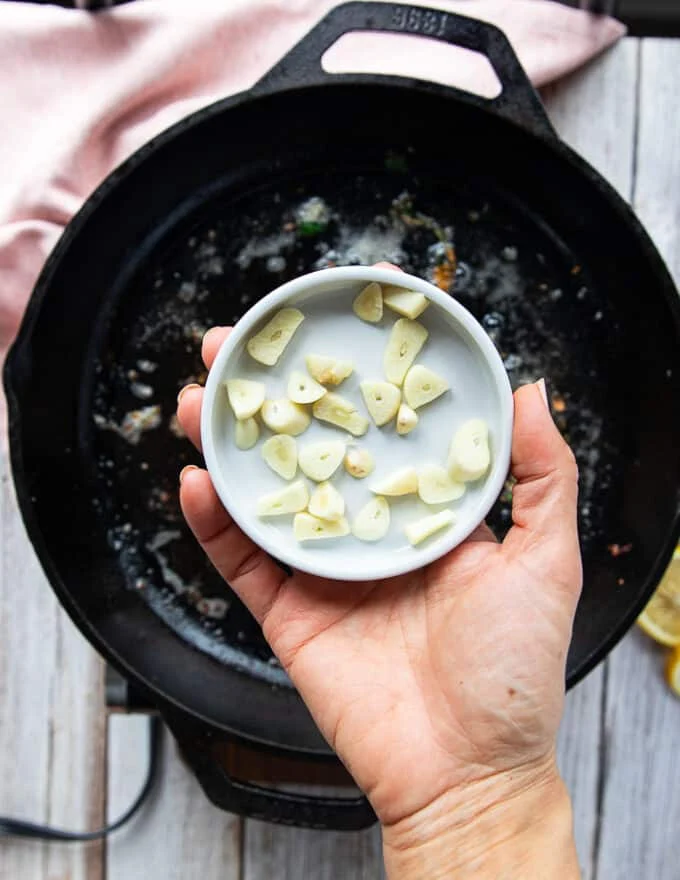 A hand holding sliced garlic ready to be added in to the same pan to make scmapi sauce