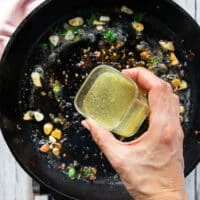 A hand pouring stock/wine mixture into the pan to make the sauce
