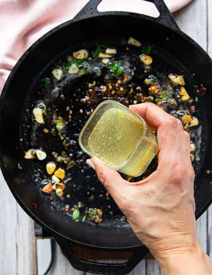 A hand pouring stock/wine mixture into the pan to make the sauce