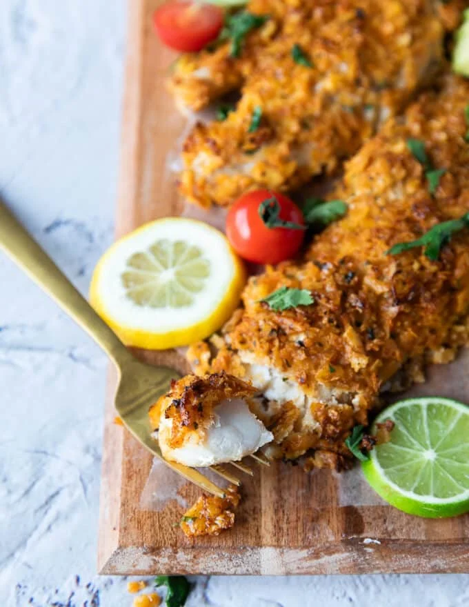 Close up of a fork holding a piece of baked haddock showing the texture of the crunchy coating and the succulent fish