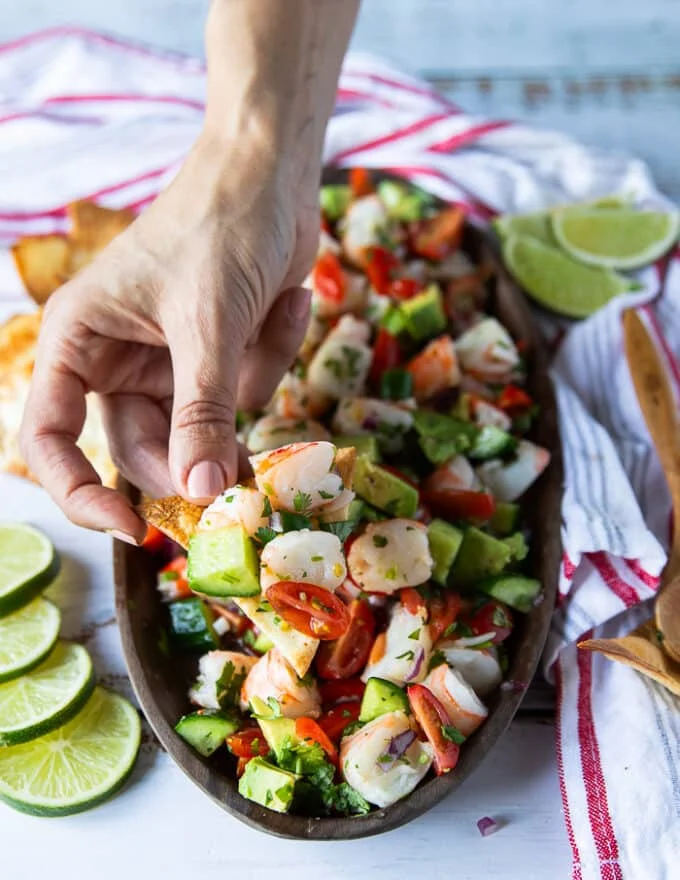 A hand holding a chip with a dip of shrimp ceviche showing close up