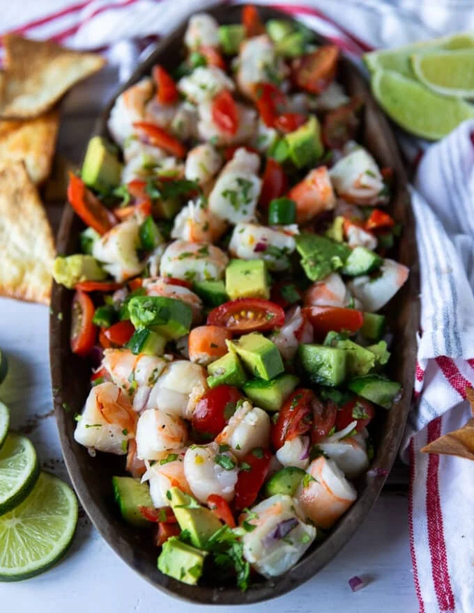 close up of a shrimp ceviche plate made up of avocados, red onions, tomatoes, cucumbers, shrimp, cilantro and surrounded by tortilla chips