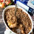 A hand scooping apple crisp showing the4 cooked soft apples and the crunchy oatmeal crumb on top