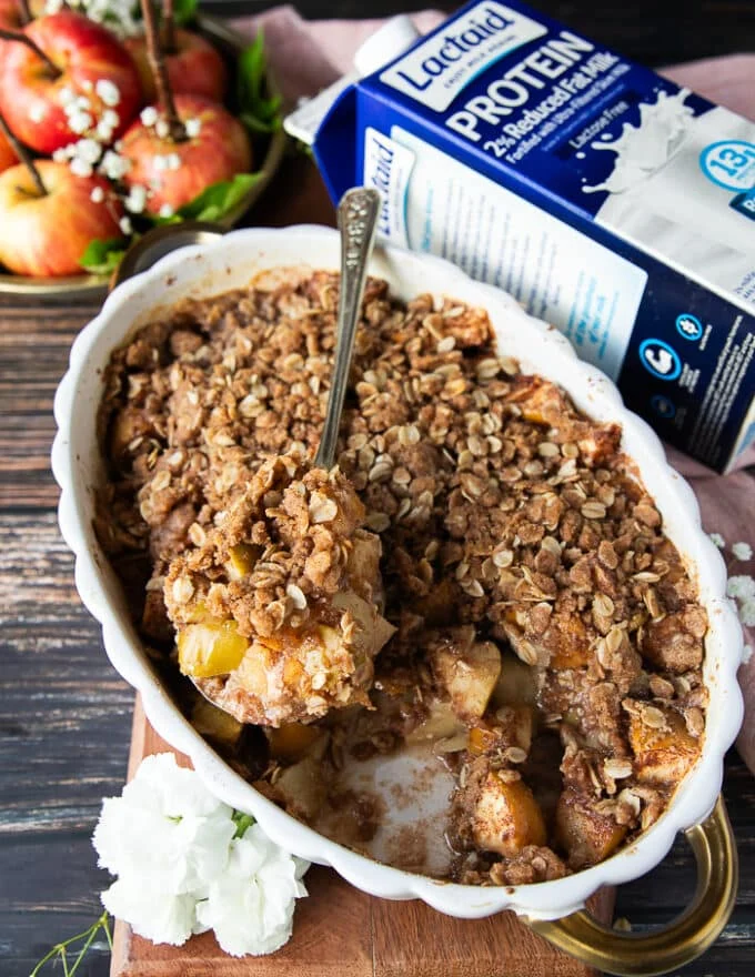 A hand scooping apple crisp showing the4 cooked soft apples and the crunchy oatmeal crumb on top