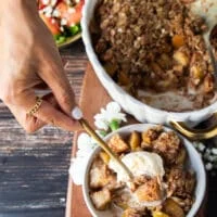 A hand holding a spoonful of apple crisp with melted vanilla ice cream over the spoon ready to eat