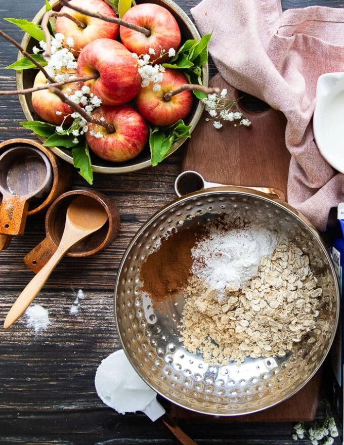 The ingredients to make the oat topping for the apple crisp on a board including oats, sugar, flour, cinnamon, butter