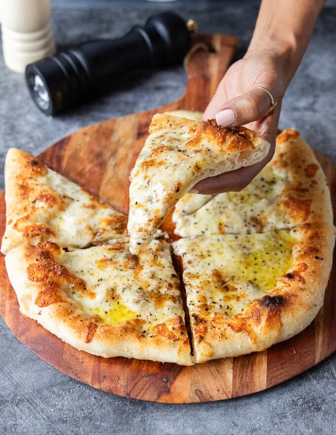 A hand holding a slice of cacio e pepe pizza showing the black pepper and pecorino cheese