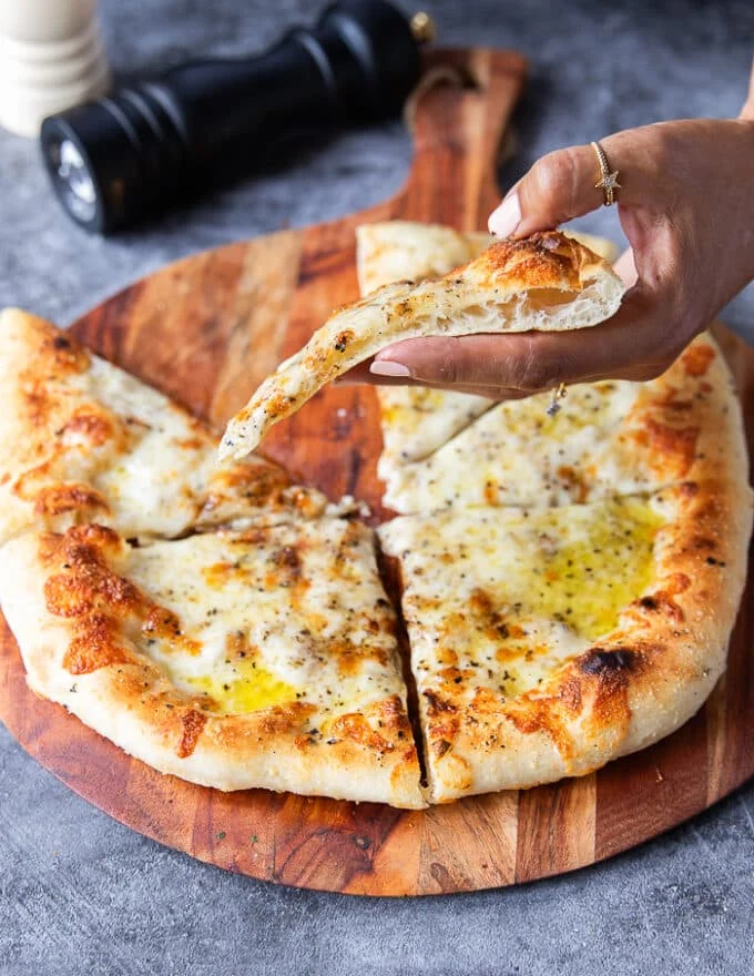 A hand holding a slice of pizza side ways showing the crust