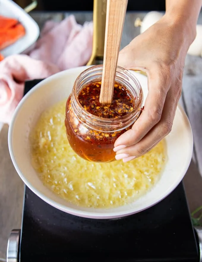 A hand holding the hot honey recipe and ready to pour it over the butter and garlic