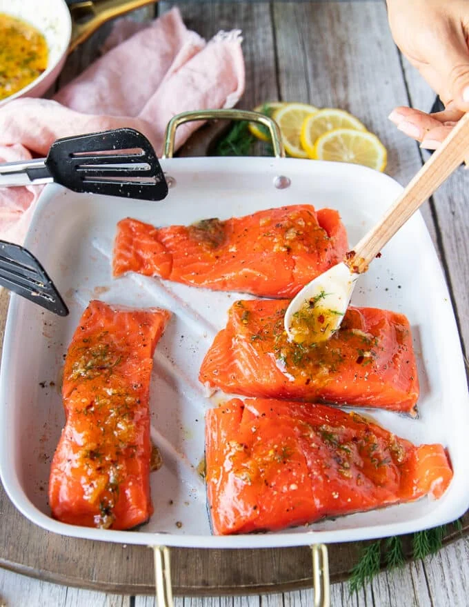 A hand pouring the glaze over the salmon before baking