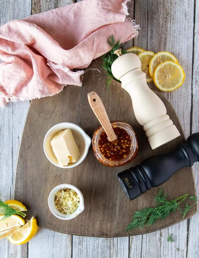 ingredients for the honey glaze in a wooden board. A hot honey recipe, butter, garlic, lemon, salt and pepper, dill, soy sauce