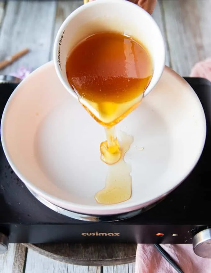 A hand pouring some honey into a sauce pan