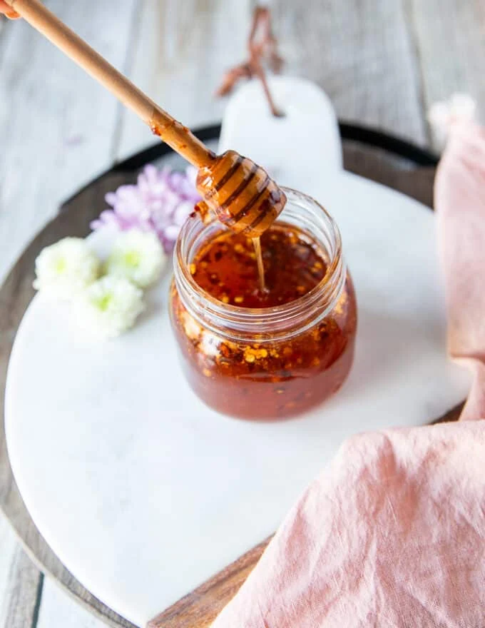 A jar of hot honey and a honey dipper showing the hot honey dripping in the jar