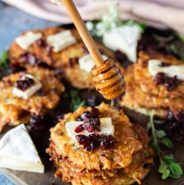 A hand drizzling honey over a stack of potato pancakes