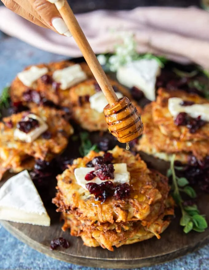 A hand drizzling honey over a stack of potato pancakes