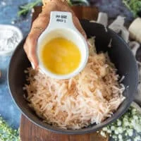 A hand holding an egg and pouring it over the squeezed potatoes and onions in a new bowl