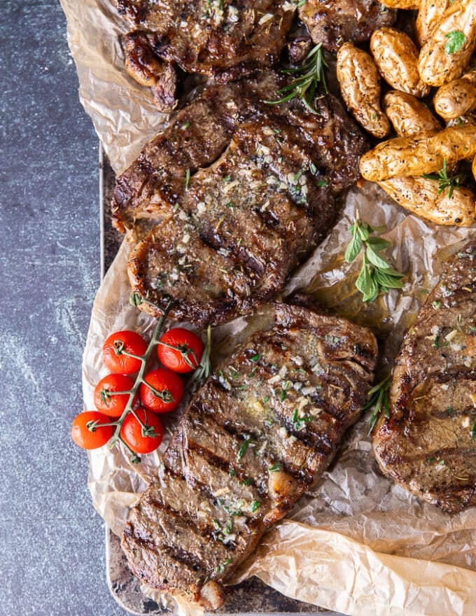 ribeye steaks on a board with some tomatoes on the side