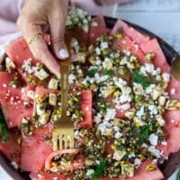 A spoon taking a chunk serving of watermelon carpaccio with the topping and everything showing close up details