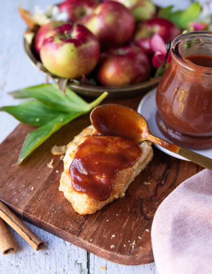 A hand holding a spoon and spreading apple butter over a croissant