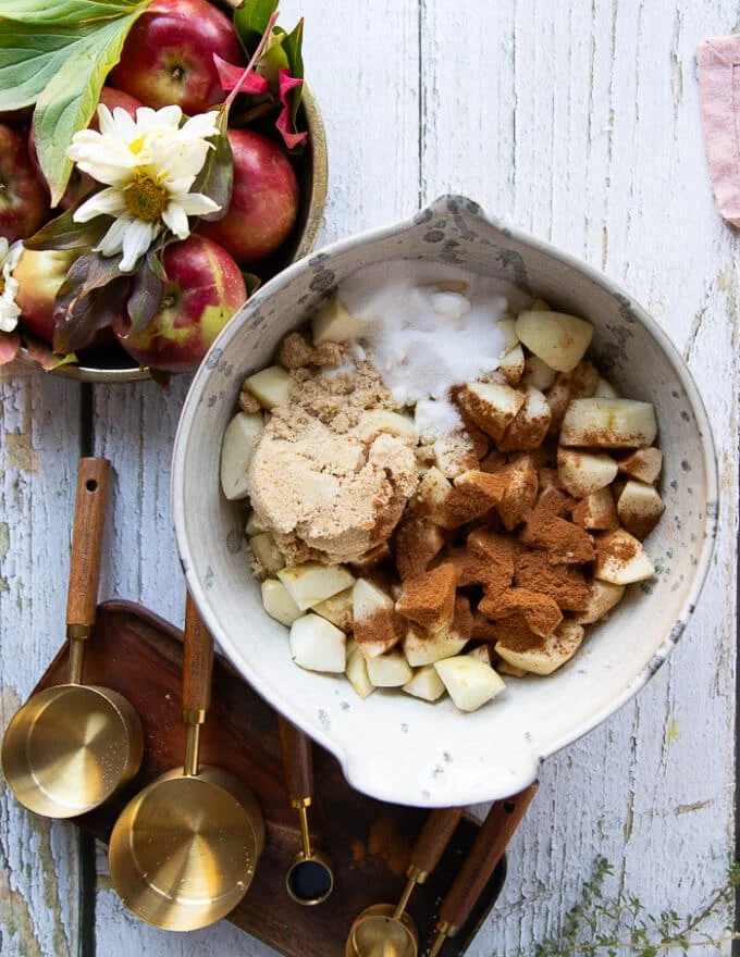 The apple butter ingredients: white sugar, brown sugar, cinnamon and salt added to the bowl of diced apples.