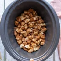 The apple mixture added to the bowl of a crockpot and set to slow cook.
