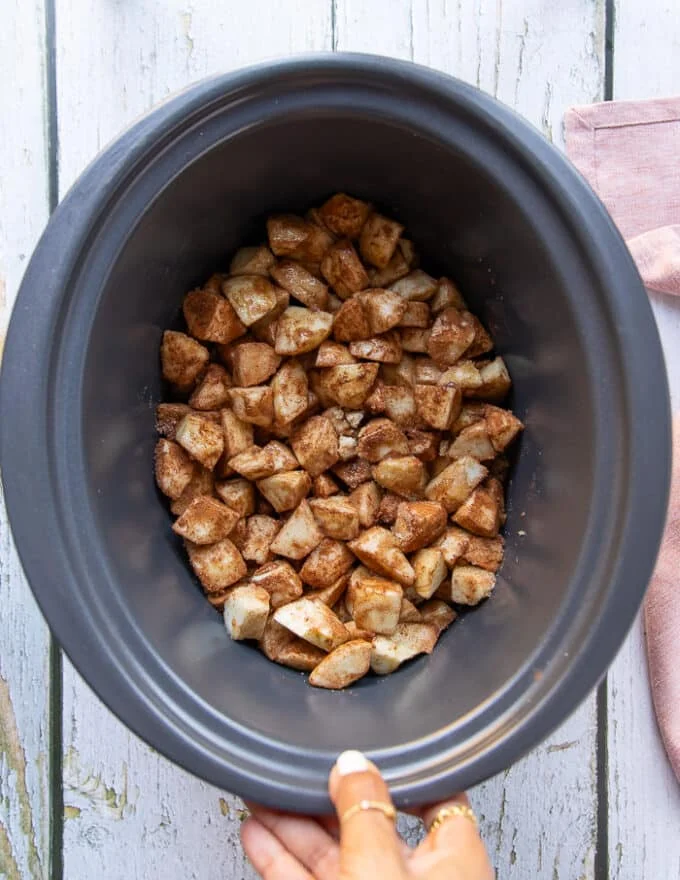 The apple mixture added to the bowl of a crockpot and set to slow cook.