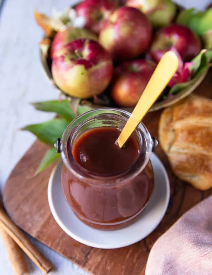 Finished apple butter placed in a glass jar with a spoon in the middle