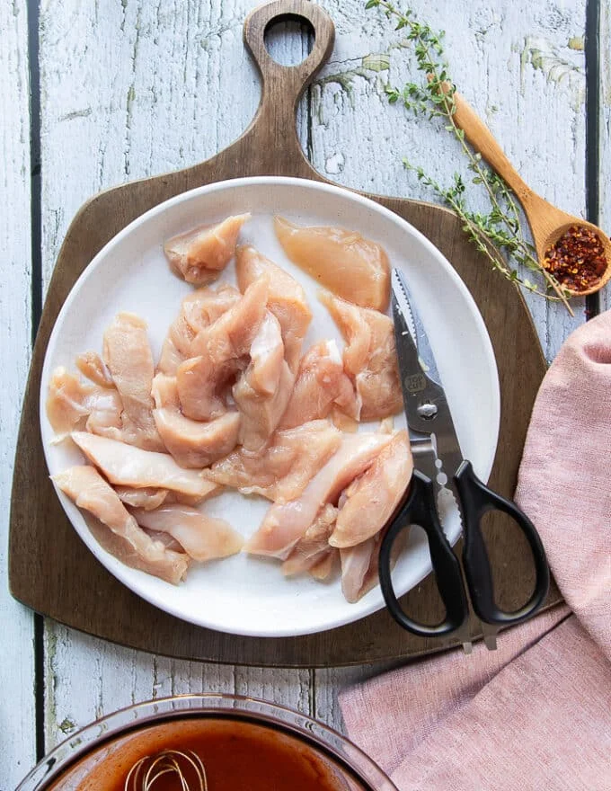 Chicken breasts cut up into strips on the plate using scissors shown next to the plate