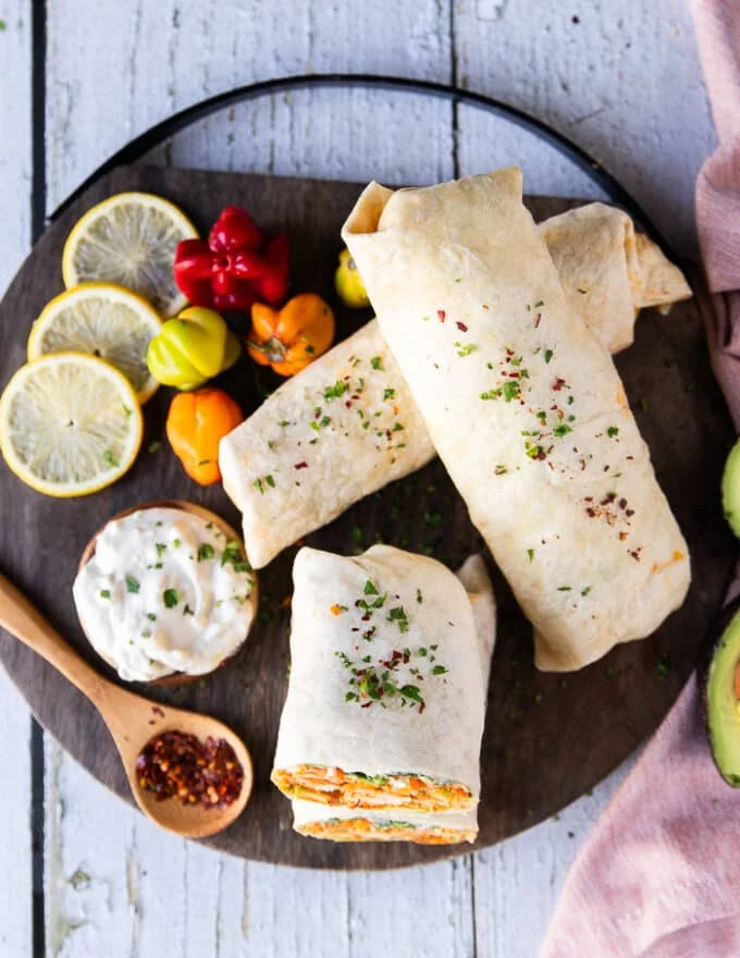 buffalo chicken wraps on a cutting board surrounded by a blue cheese dip for extra dipping and some chilli flakes