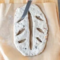 The knife making diagonal slits on both sides of the dough to create the classic leaf shape