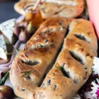 One Fougasse bread on a white board close up showing the add ins and the golden bread shaped like a leaf