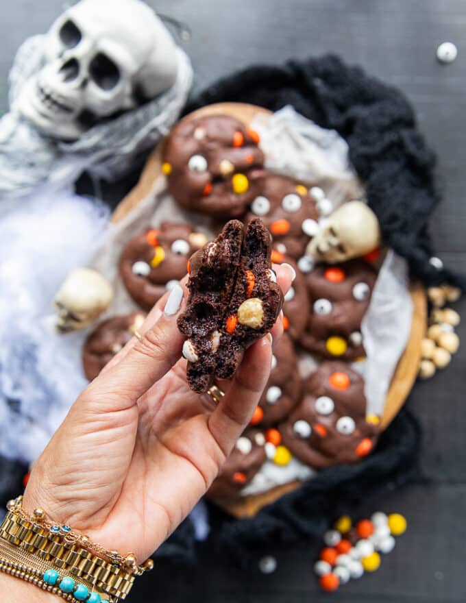 A hand holding a halloween cookies broken in half showing the soft inside of the cookie