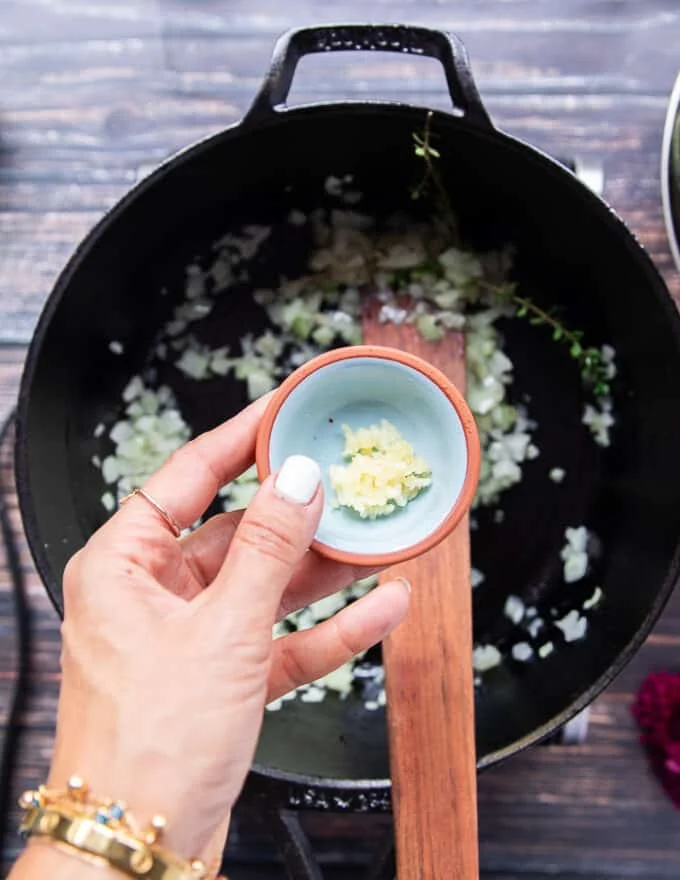 A hand holding a bowl of minced onions ready to add in the pot of risotto