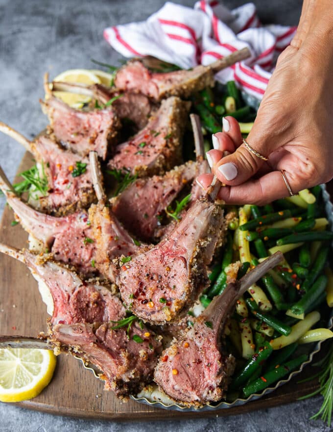 A hand holding a piece of lamb chop cut off from the rack of lamb to show the doneness