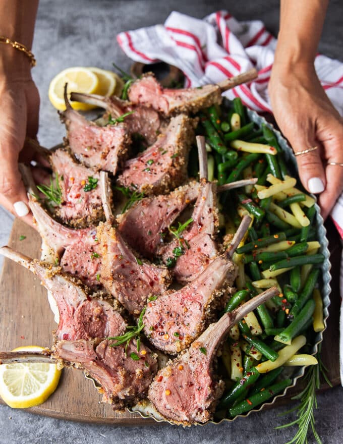 A hand holding a platter of sliced rack of lamb served next to steamed green beans