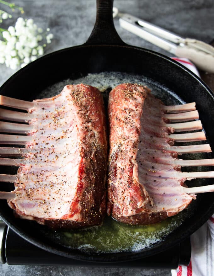 two french cut racks of lamb searing in a pan with melted butter