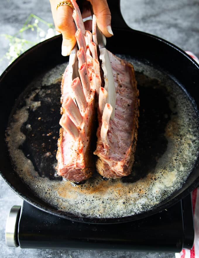 The rack of lamb is held straight to get all sides of it seared