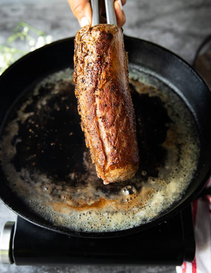 Final seared rack of lambs with a golden crisp buttery crust shown close up and placed on a rack