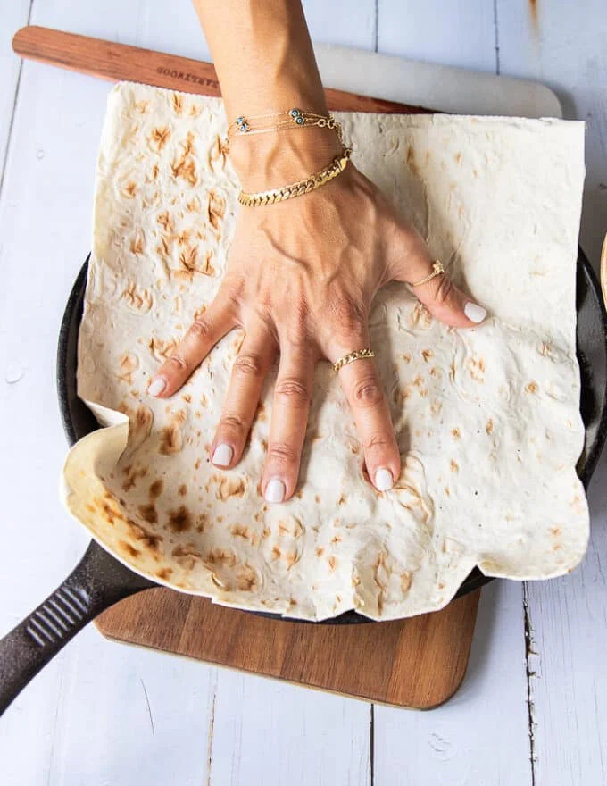 A hand pressing down the lavash bread over the cooked meat in the skillet with spices and sauce to flavor the bread for tantuni