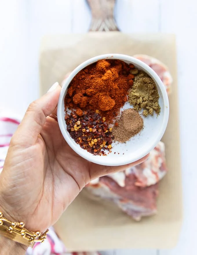 A hand holding a spice blend for the lamb including, Pul Biber, paprika, chilli flakes, cumin, nutmeg, salt and pepper